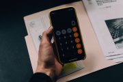 Hand holding an iPhone with the calculator app open and a folder of documents on the table: Planning your personal finances is a crucial first step towards buying a home